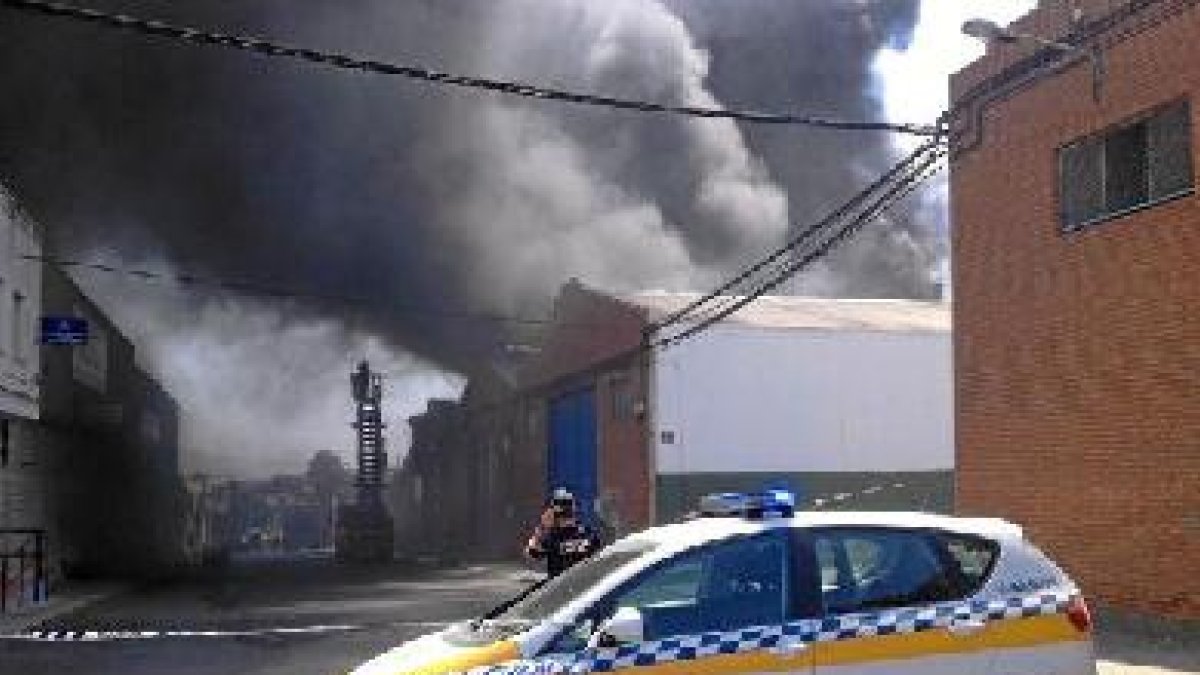 Un coche de policía impide el acceso al perímetro de la nave siniestrada, mientras los bomberos trab