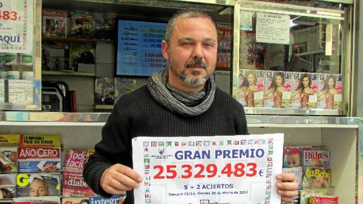 El quiosquero Juan Carlos Andújar Lazo posa junto al cartel que anuncia la cifra del premio que ha