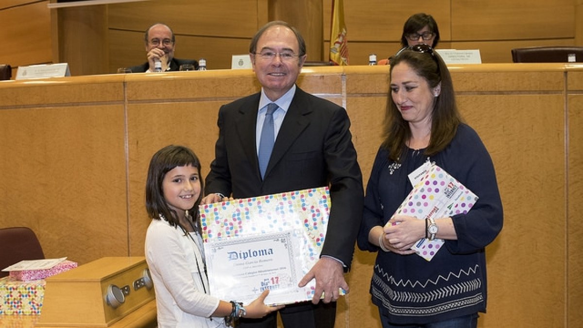 El presidente  del Senado, Pío García Escudero, entregando el premio a Emma, junto a su profesora Ángeles González.