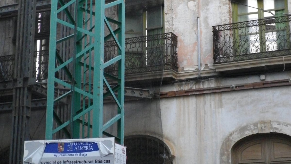 Grúa ante la fachada del edificio en la que se puede ver el cartel con datos de la obra.