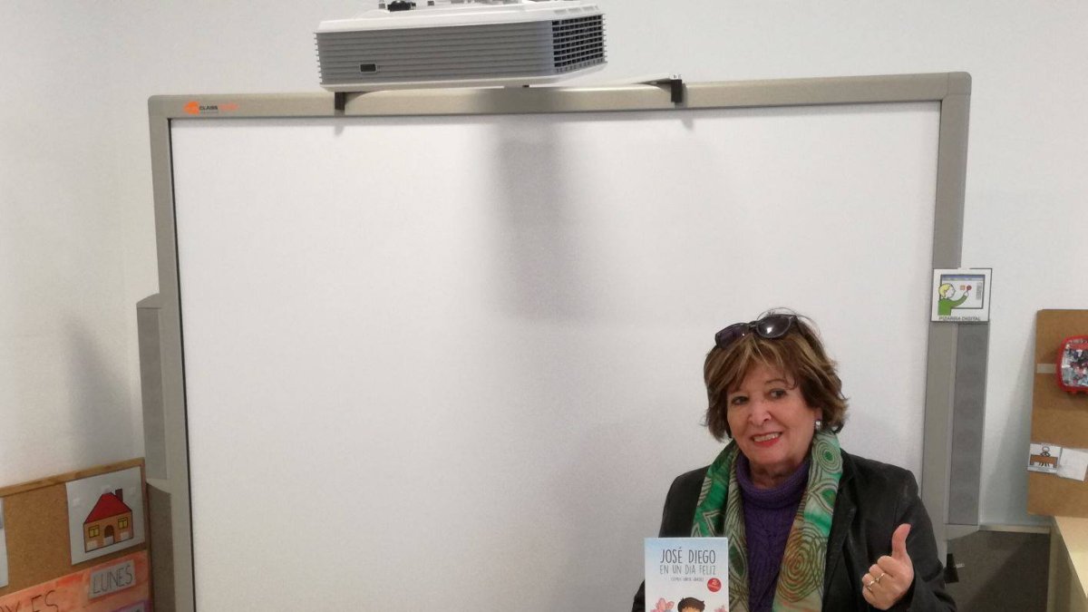 Clementina y su nieto posan frente a la pizarra y con el cuento solidario.