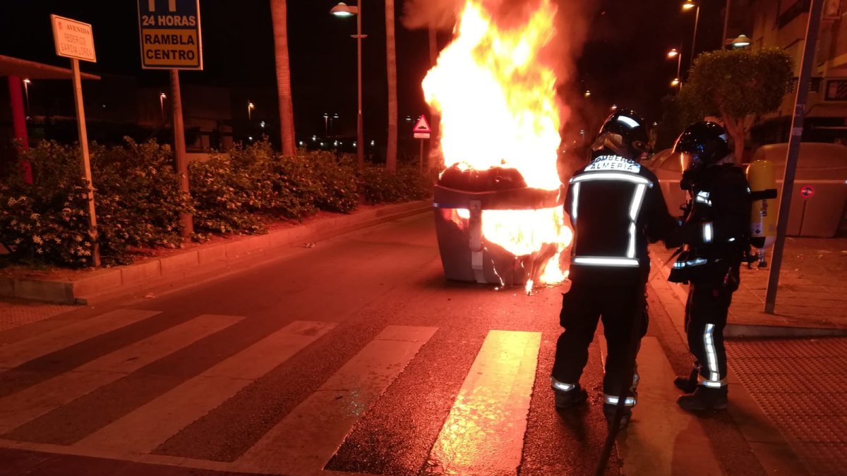 Efectivos del cuerpo de bomberos haciendo frente a las llamas de un contenedor urbano en una calle de la capital.