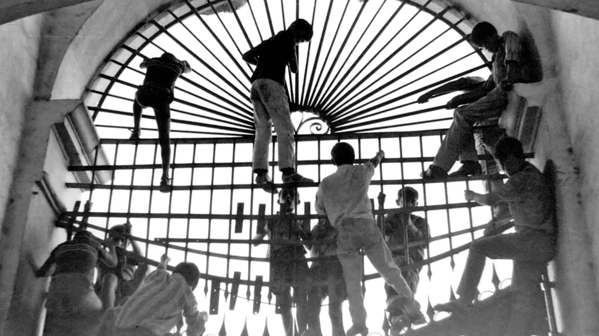 un grupo de muchachos escalando por las rejas de la Plaza de Toros en busca de un resquicio por donde poder colarse.