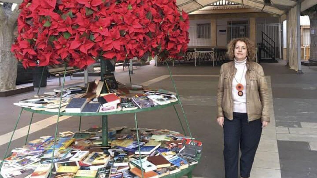 La concejal de Cultura junto al árbol instalado en la Plaza de la Constitución con los libros.