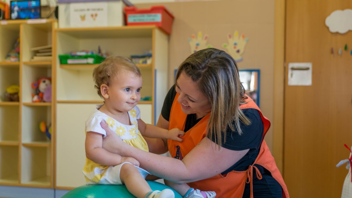 Una niña realiza ejercicios de estimulación bajo la atenta mirada y el apoyo de una educadora