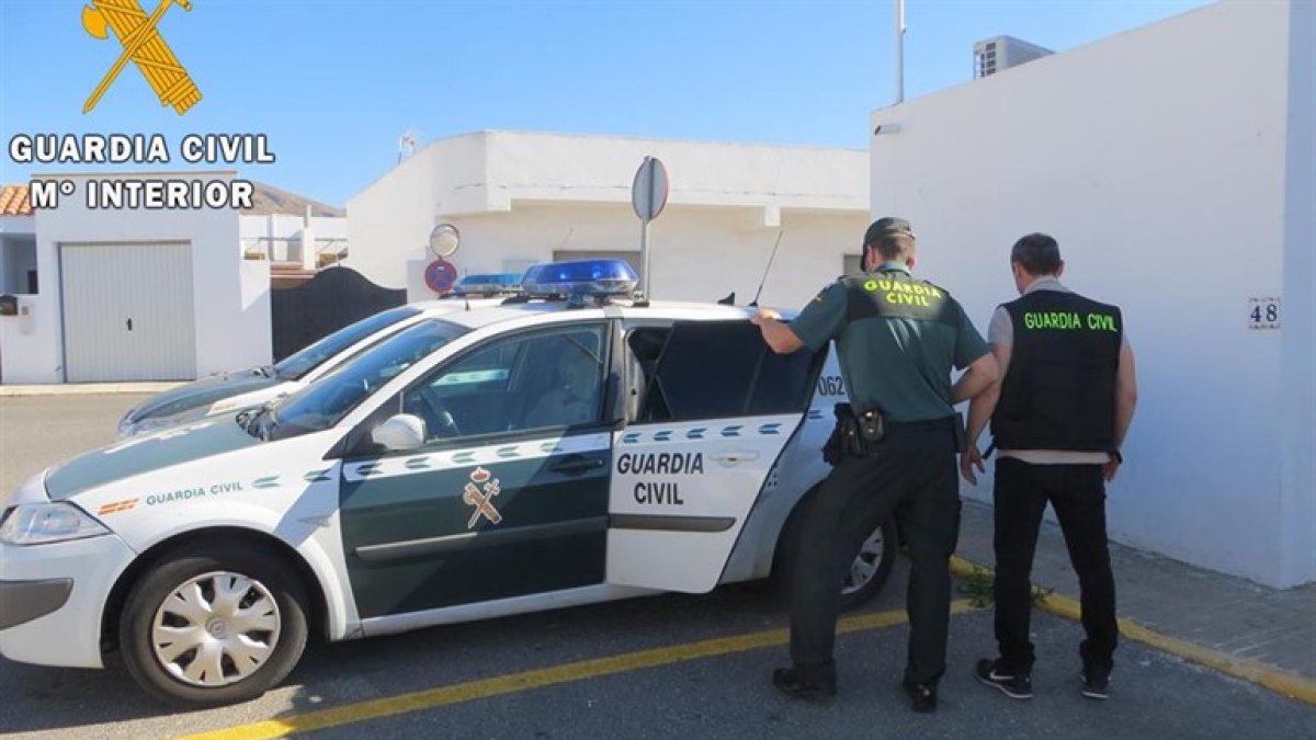 Dos Guardias Civiles meten a un detenido en el coche patrulla.