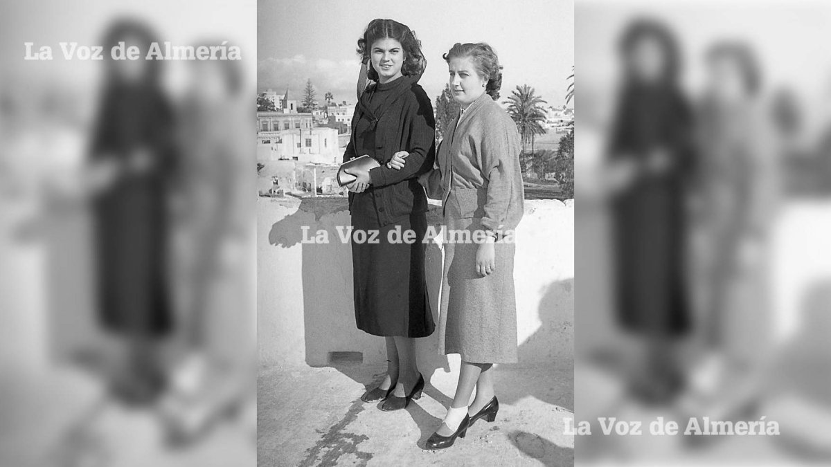 Dos muchachas vestidas de domingo. Una iba con su indumentaria de ir a misa. Al fondo se ve la torre de la antigua iglesia de San José.