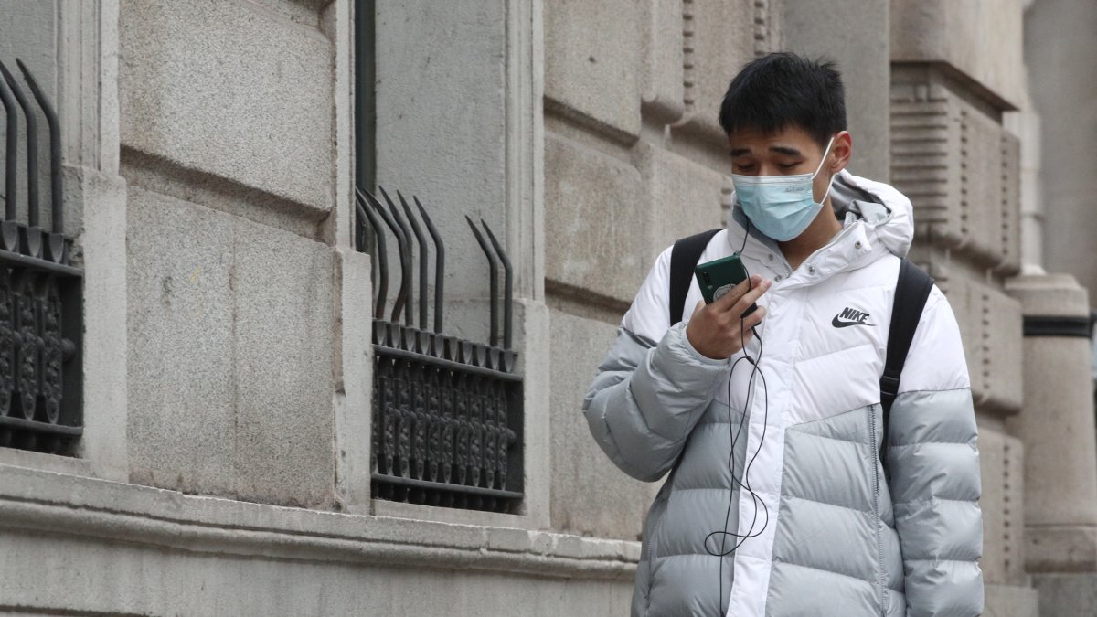 Un asiático pasea por la calle con una mascarilla.