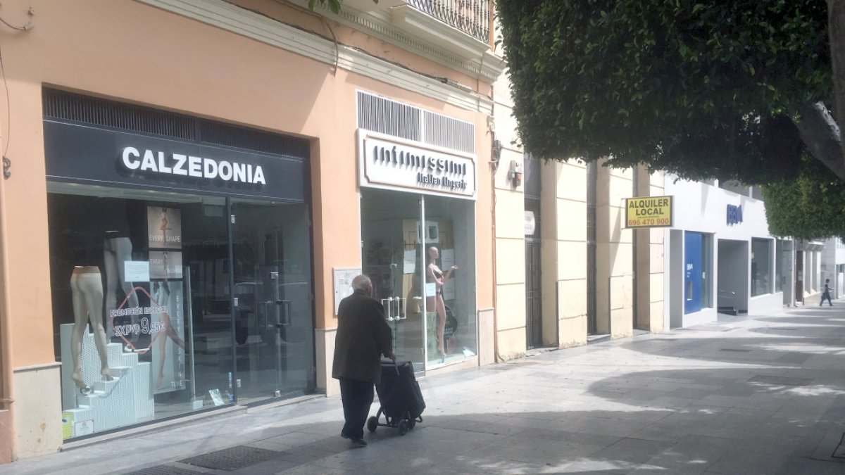 Un señor con su carrito de la compra, atravesando ayer el Paseo solitario, junto a unos establecimientos de venta de prendas íntimas.