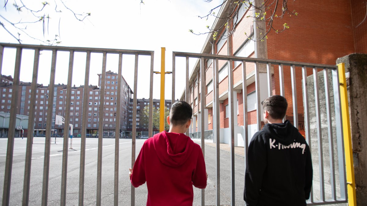 Dos adolescentes observan el patio cerrado de un colegio durante el confinamiento por el estado de alarma.