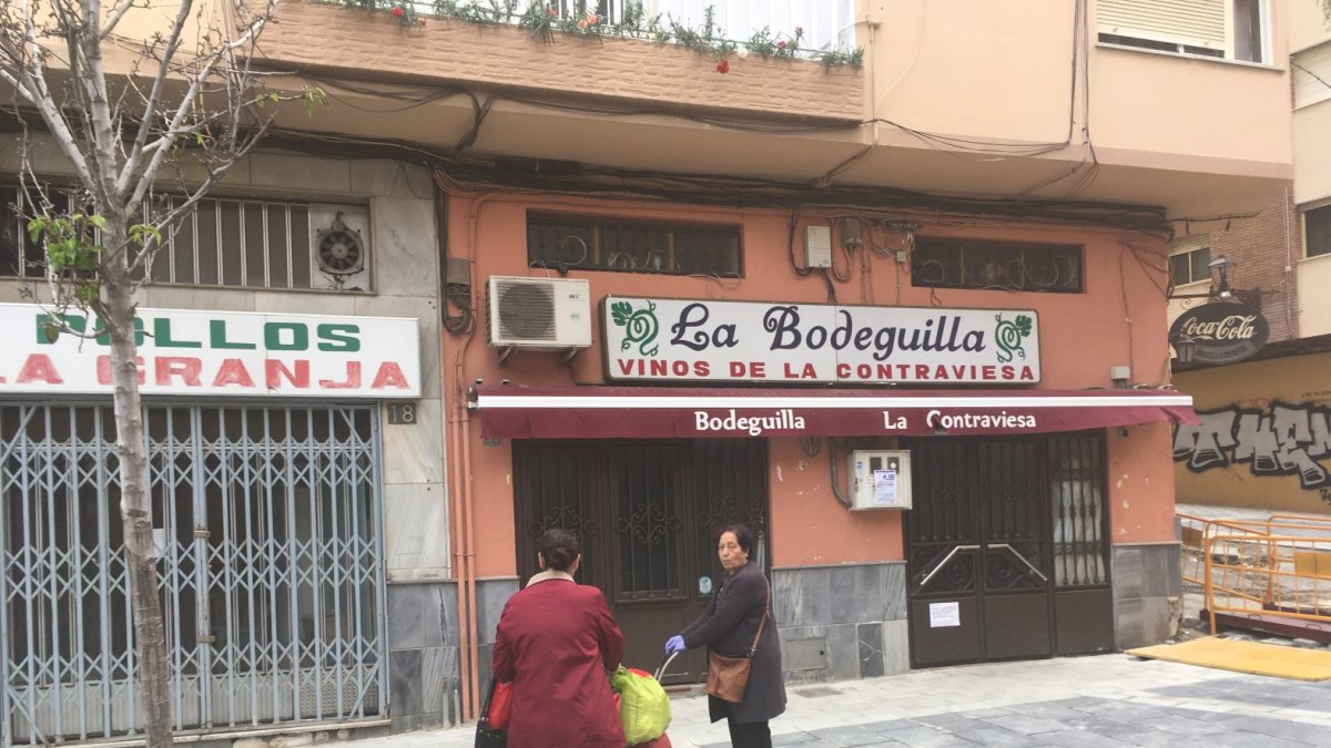 Dos señoras saludándose en la calle Trajano. Parecen estar poniéndose al día, cargadas de alimentos, frente a la Bodeguilla y Pollos La Granja.