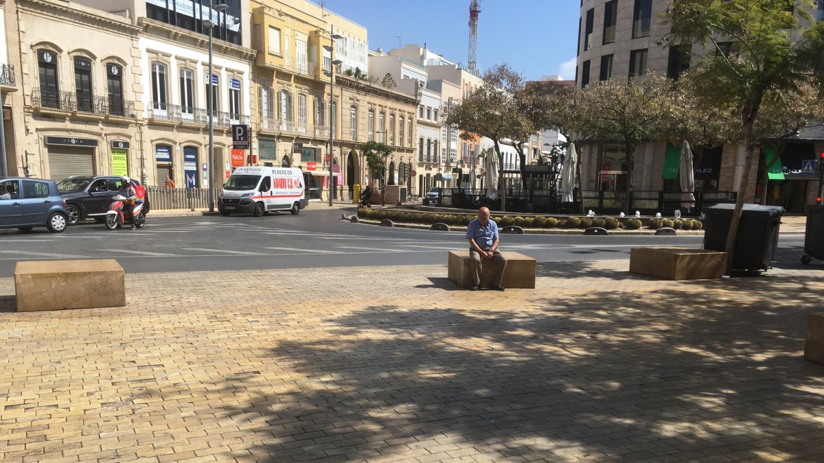 Un hombre sentado y solitario en un banco de piedra de la Puerta Purchena. Detrás, el centro de la ciudad que empieza a desperezarse.
