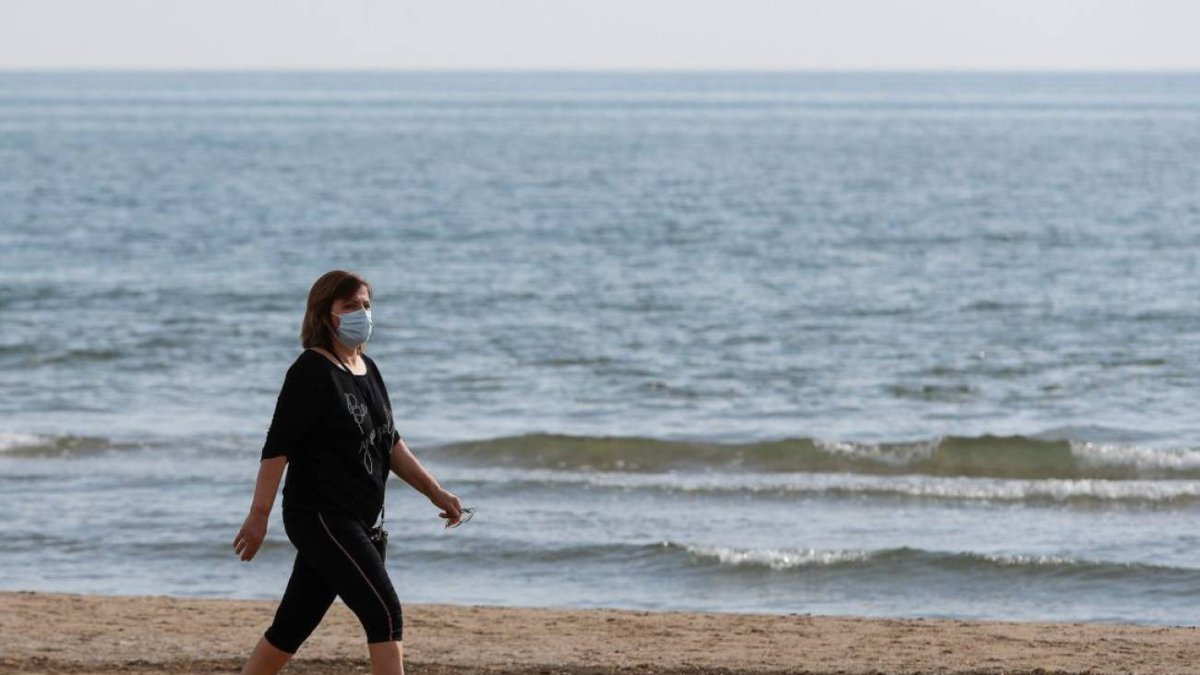 Una mujer con mascarilla pasea por la playa de la Malvarrosa / Iván Terrón.