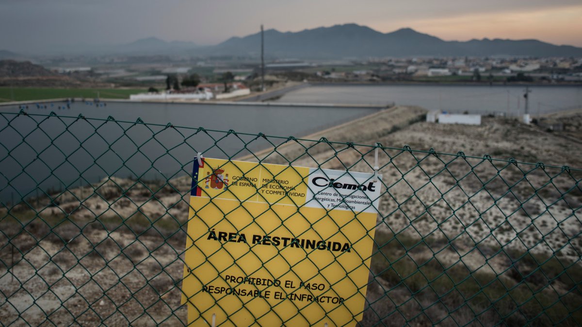Vala que acota el área contaminada, con el puerto al fondo.