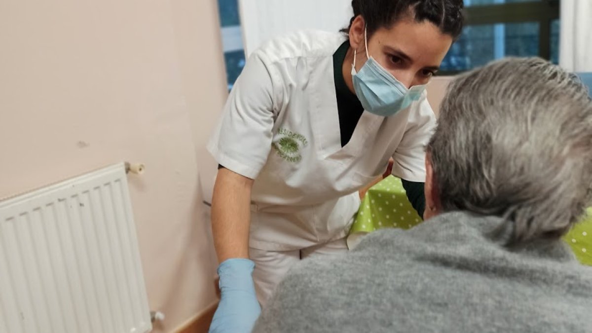 Una residente en un geriátrico atendida por una profesional con mascarilla.