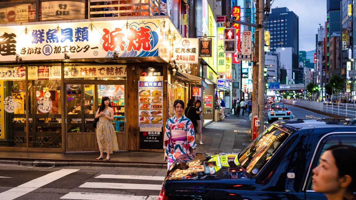 Intersección de calles repleta de luminosos mientras una joven con kimono cruza un paso de cebra (Foto: Chema Artero).