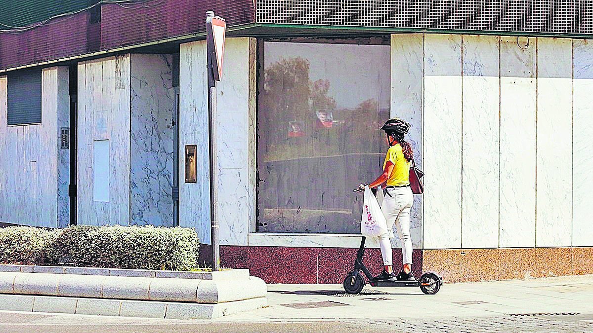 Imagen de archivo de una mujer utilizando un patinete eléctrico por la acera.