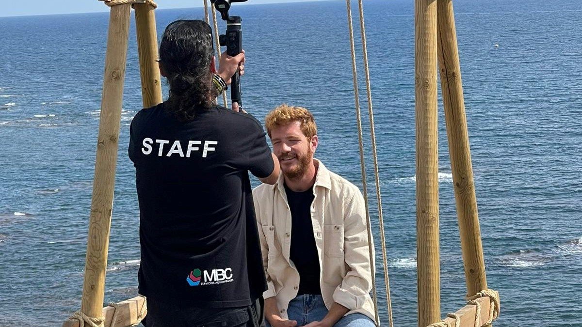 Juanlu González graba sentado en el columpio instalado en Cala Invencible.