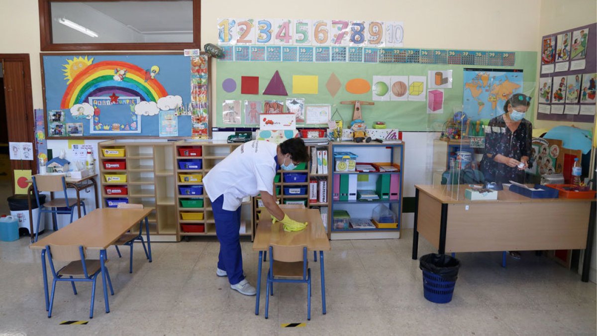 Una profesional limpia un aula educativa.