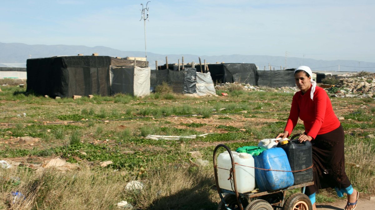 Una mujer transporta envases con agua entre chabolas de El Ejido.