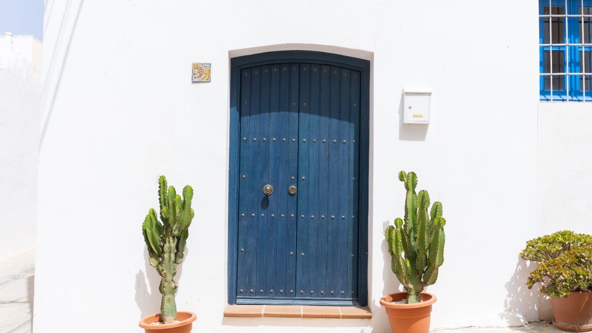 Una casita de fachada blanca y ventanas y puertas azules.