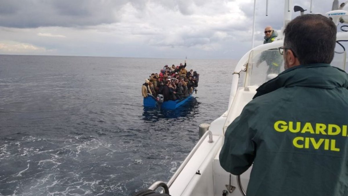 Un guardia civil observa una patera con inmigrantes.