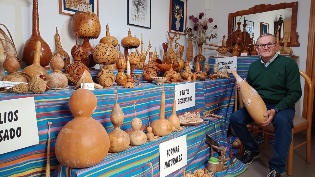 Manuel Ayala posa con su colección de tallas de calabazas desplegada en el salón de su casa.