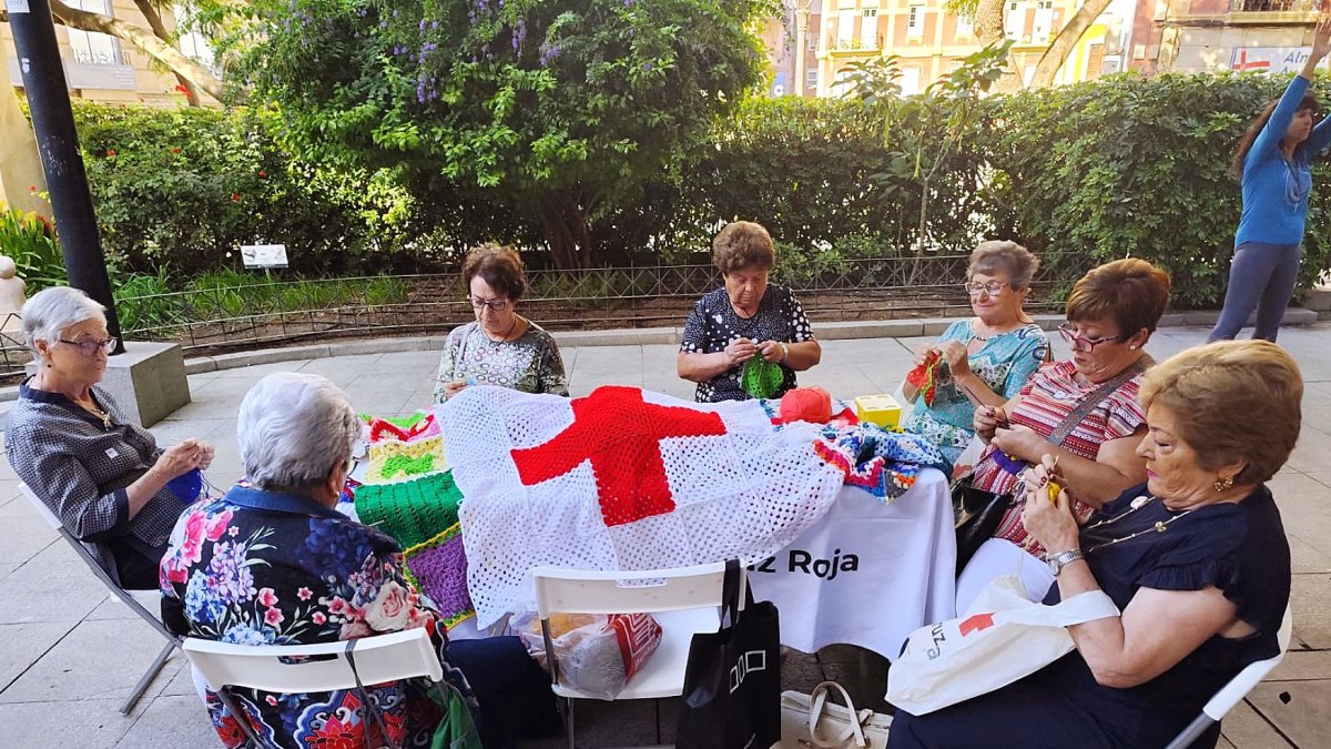Usuarias de la Cruz Roja tejen una bandera de la organización.