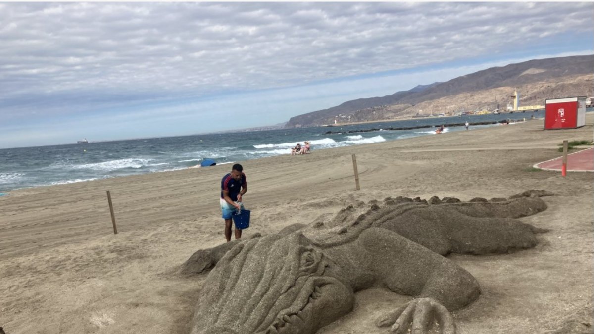 Karim refrescando a su caimán, ya desaparecido,, sobre la arena de la playa de El Zapillo.