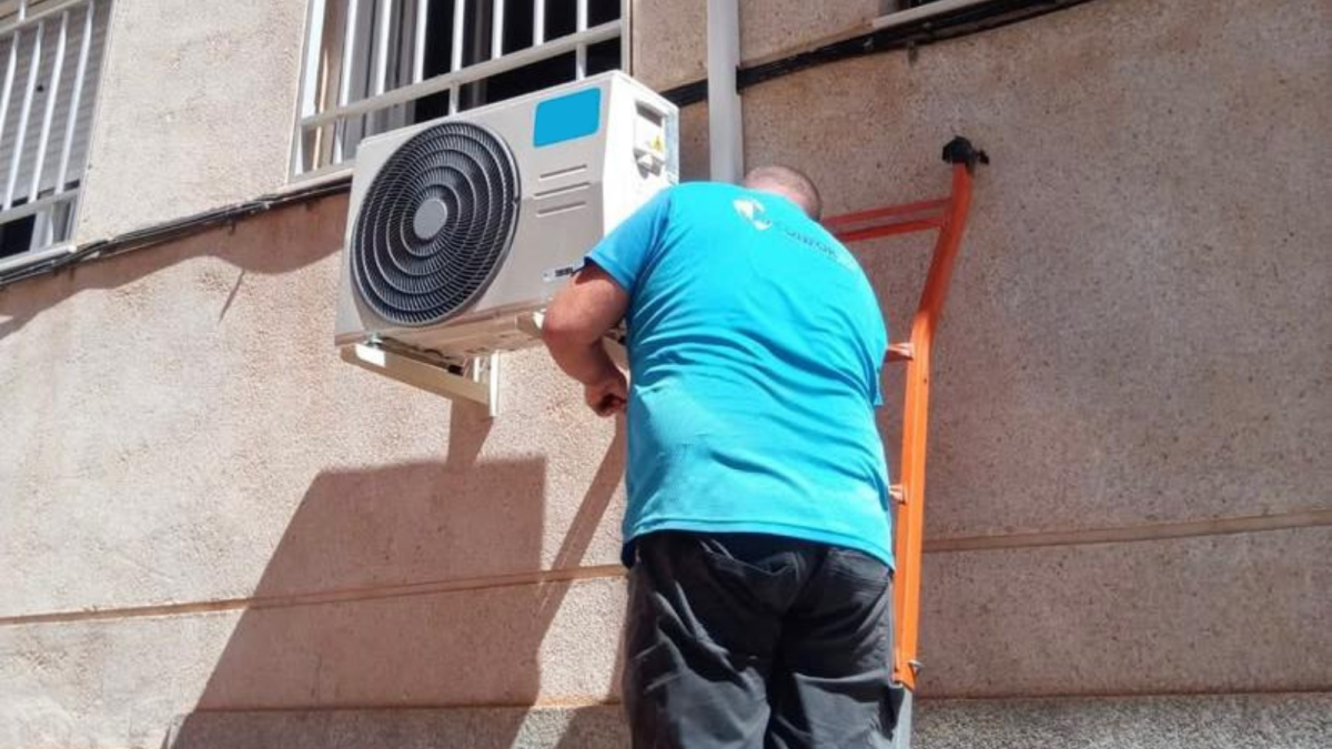Un almeriense instala un aparato de aire acondicionado a las afueras de un edificio.