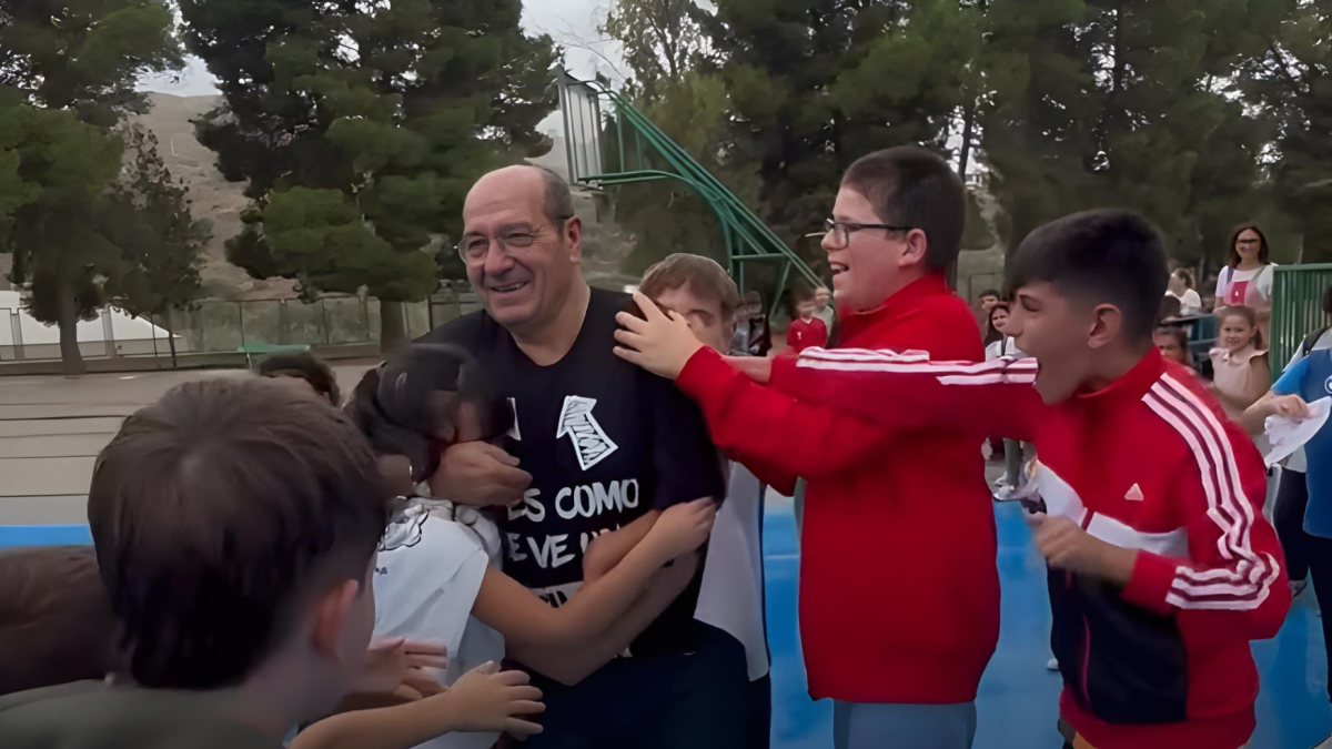Alumnos y compañeros despiden en un largo pasillo por el patio a Julián el día de su despedida.