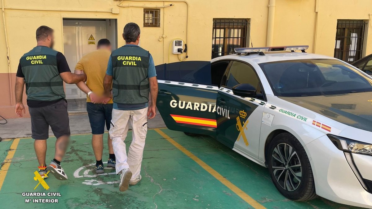 Dos guardias civiles escoltan al detenido hasta el coche oficial.