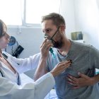 Un joven, con mascarilla de oxígeno, es auscultado por una doctora en urgencias.