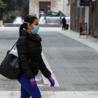 Una mujer camina con mascarilla y guantes de látex.