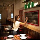 Una camarera apunta platos en una pizarra en el interior de un bar.