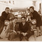 Francisco Hernández, agachado en cuclillas, con un cigarro en la mano, junto a unos clientes. Al lado se ve un antiguo surtidor de gasolina.