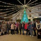 Fotografía de familia de las creadoras del árbol de ganchillo (al fondo iluminado) junto al alcalde.