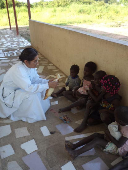 La hermana Justina Soriano Méndez ofrece una mazorca a un grupo de niños angoleños.